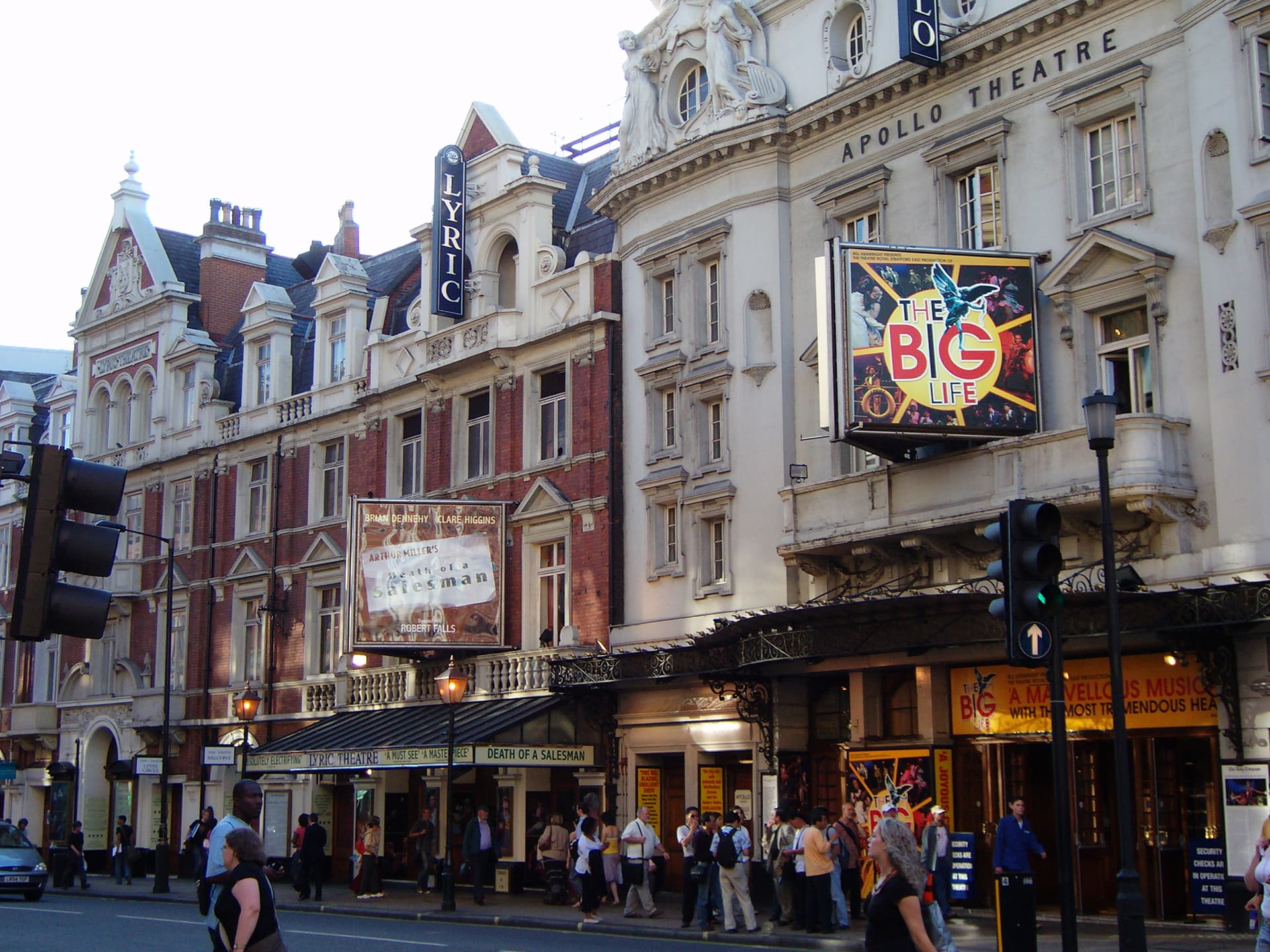 Lyric and Apollo theatre frontages on Shaftesbury Avenue, with show billboards, traffic lights and pedestrians on the pavement