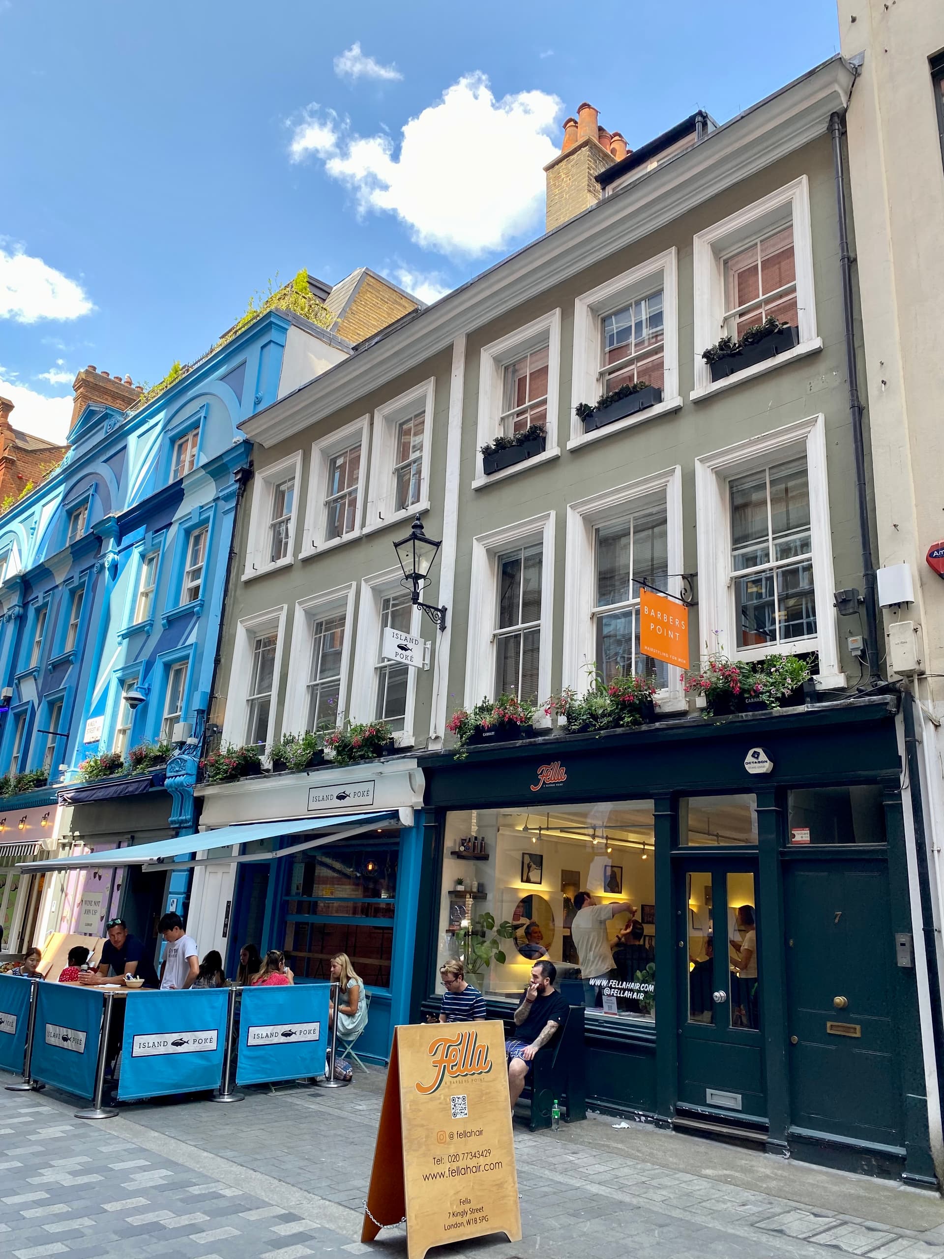 Colourful Georgian shopfronts on Kingly Street, Soho, with diners seated outside a poké restaurant beside a barbershop