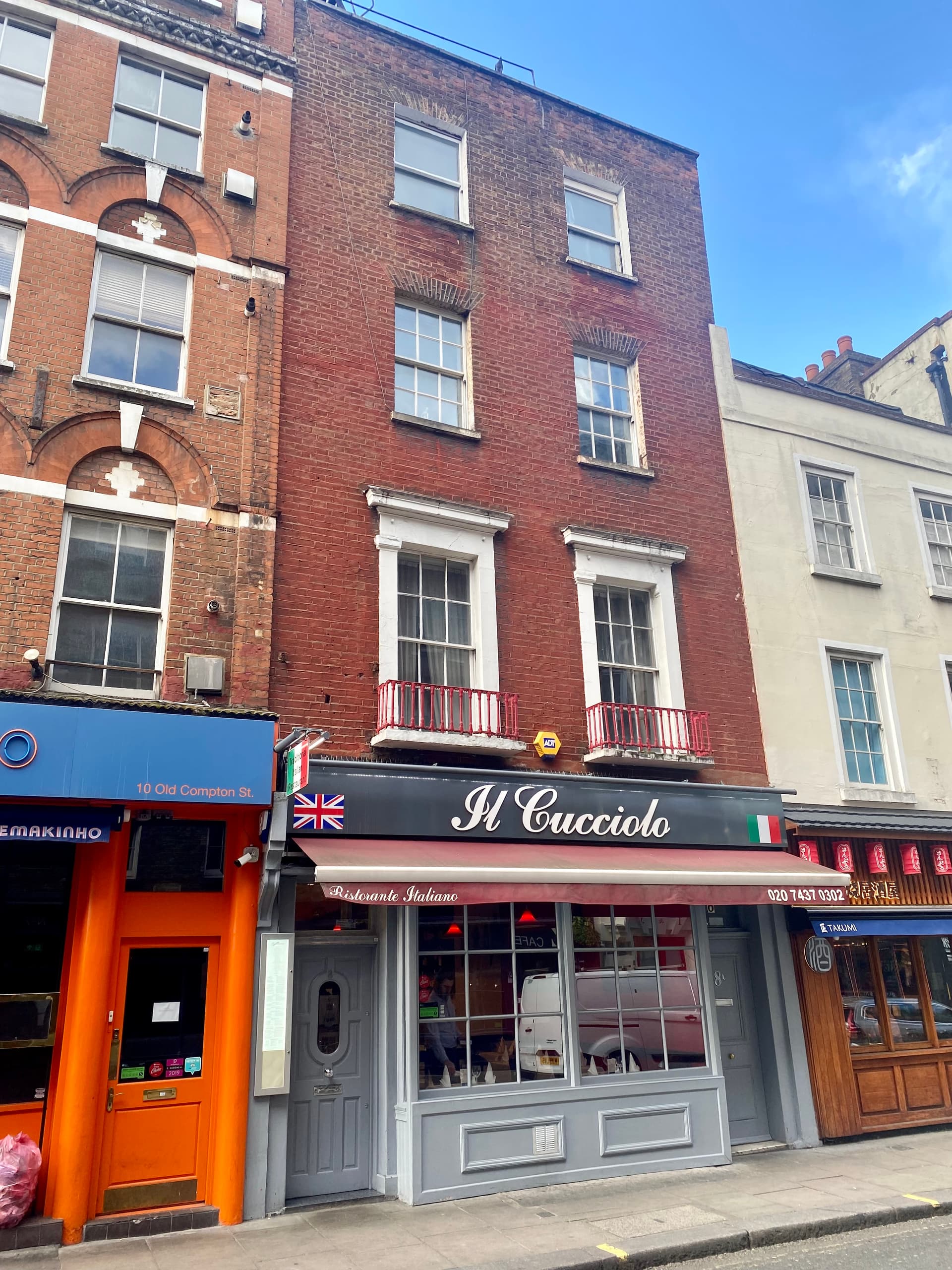 Georgian brick townhouse above Il Cucciolo Italian restaurant, between an orange shopfront and a Japanese izakaya on Old Compton Street