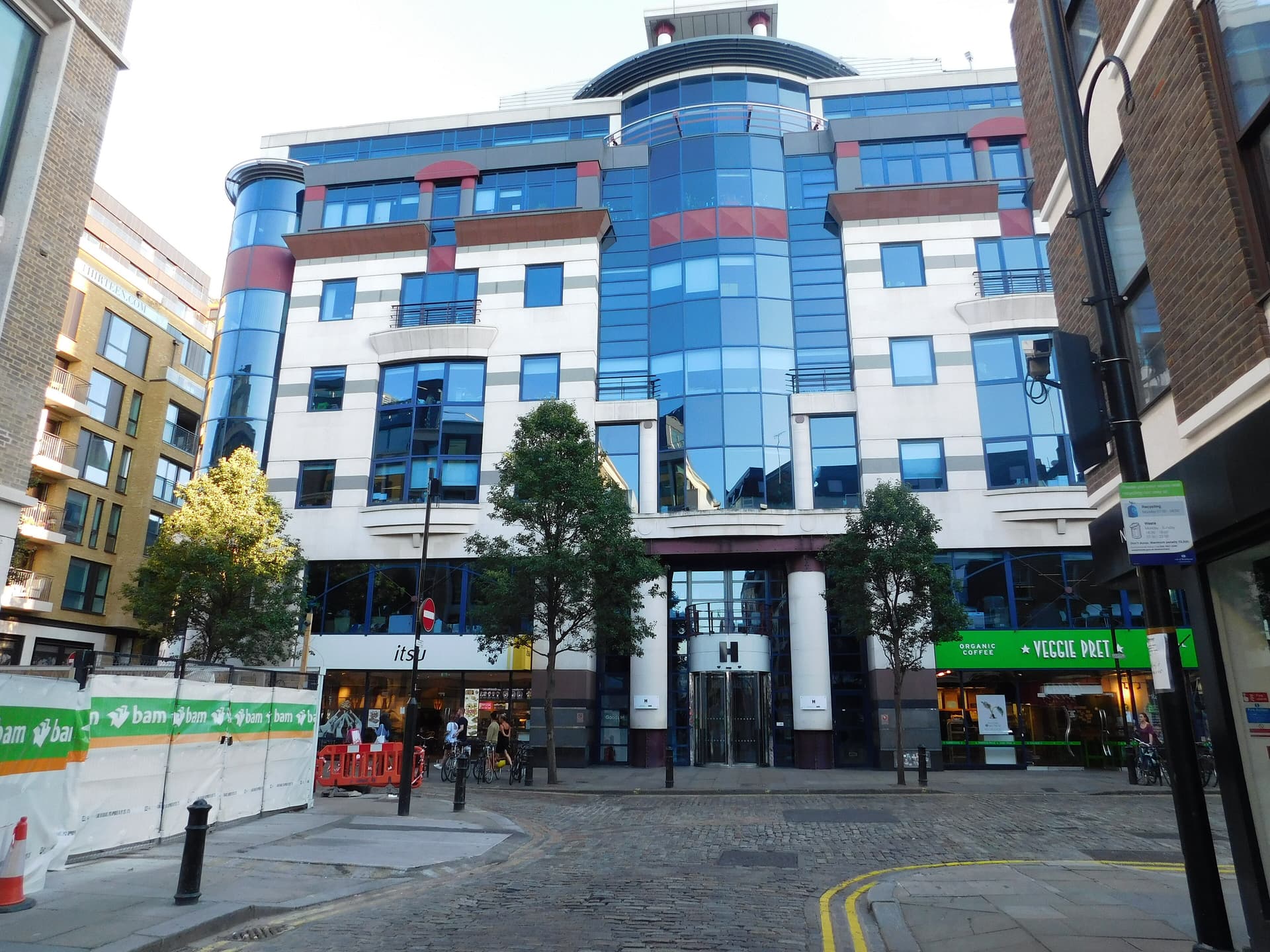 Postmodern glass and stone office building on a cobbled Soho street, with Itsu and Veggie Pret at ground level