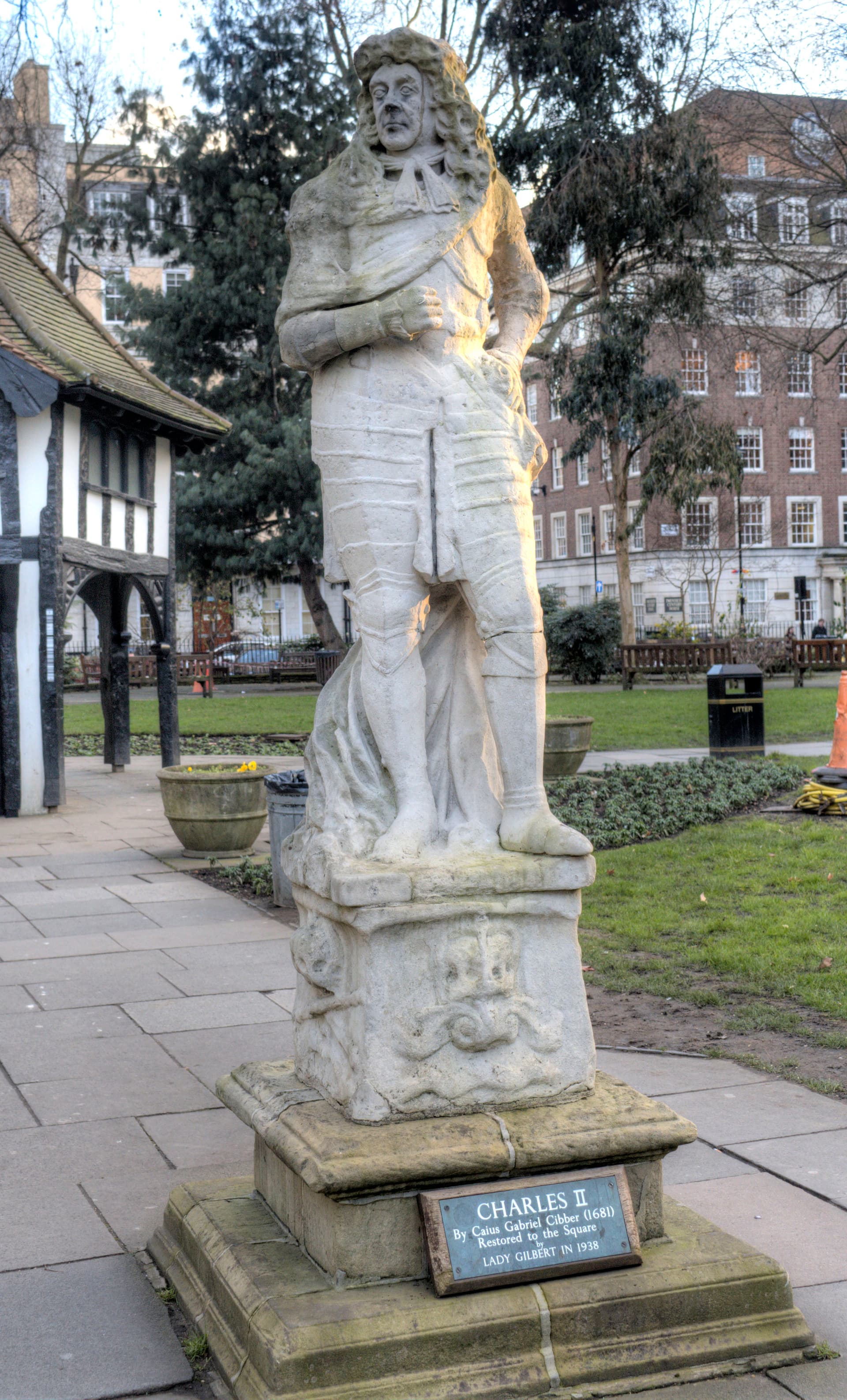 Weathered stone statue of Charles II on a plinth in Soho Square gardens beside the mock-Tudor garden hut