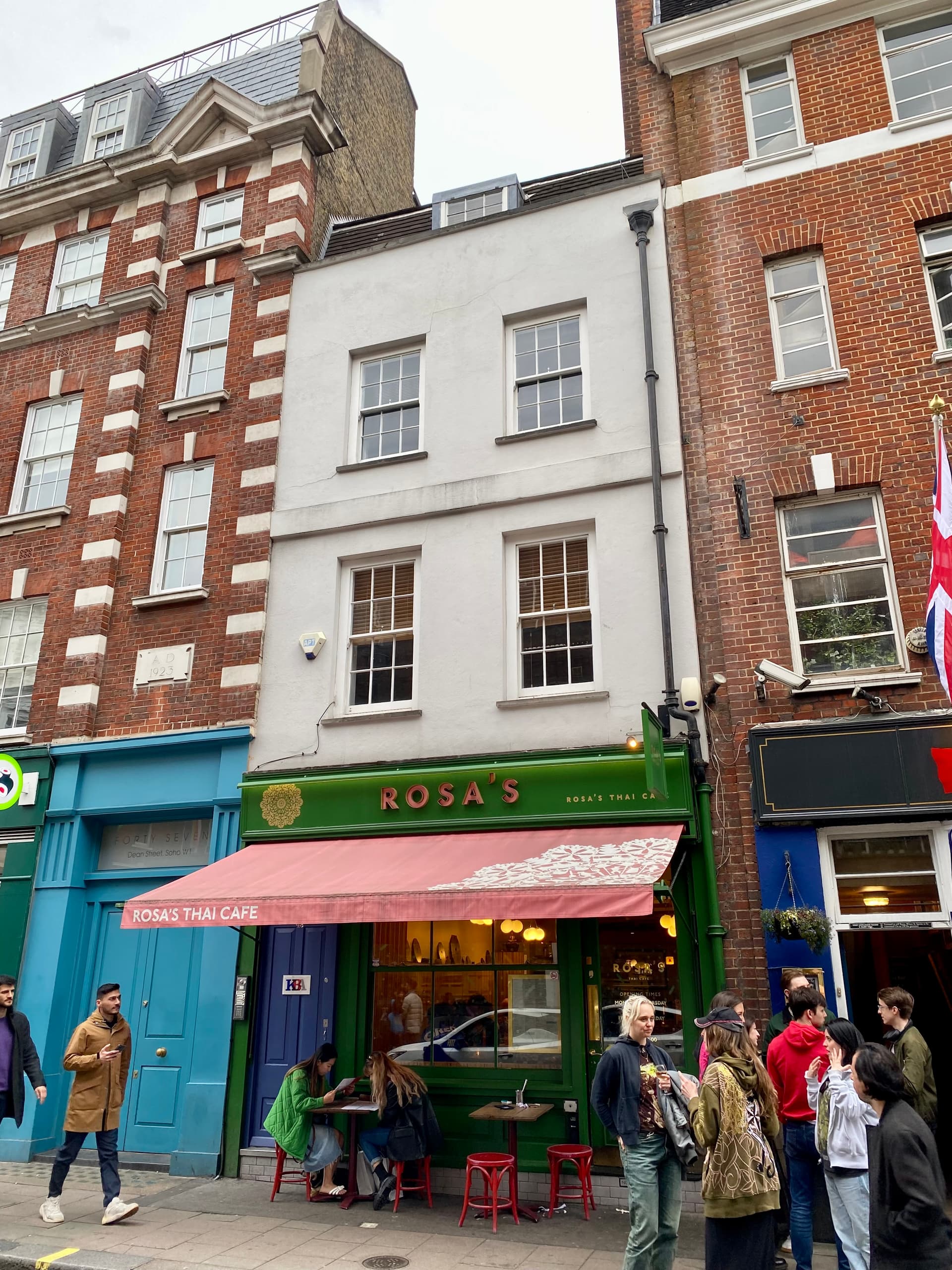 Rosa's Thai Cafe with pink awning on Dean Street, Soho, between brick and blue-painted frontages, pedestrians outside