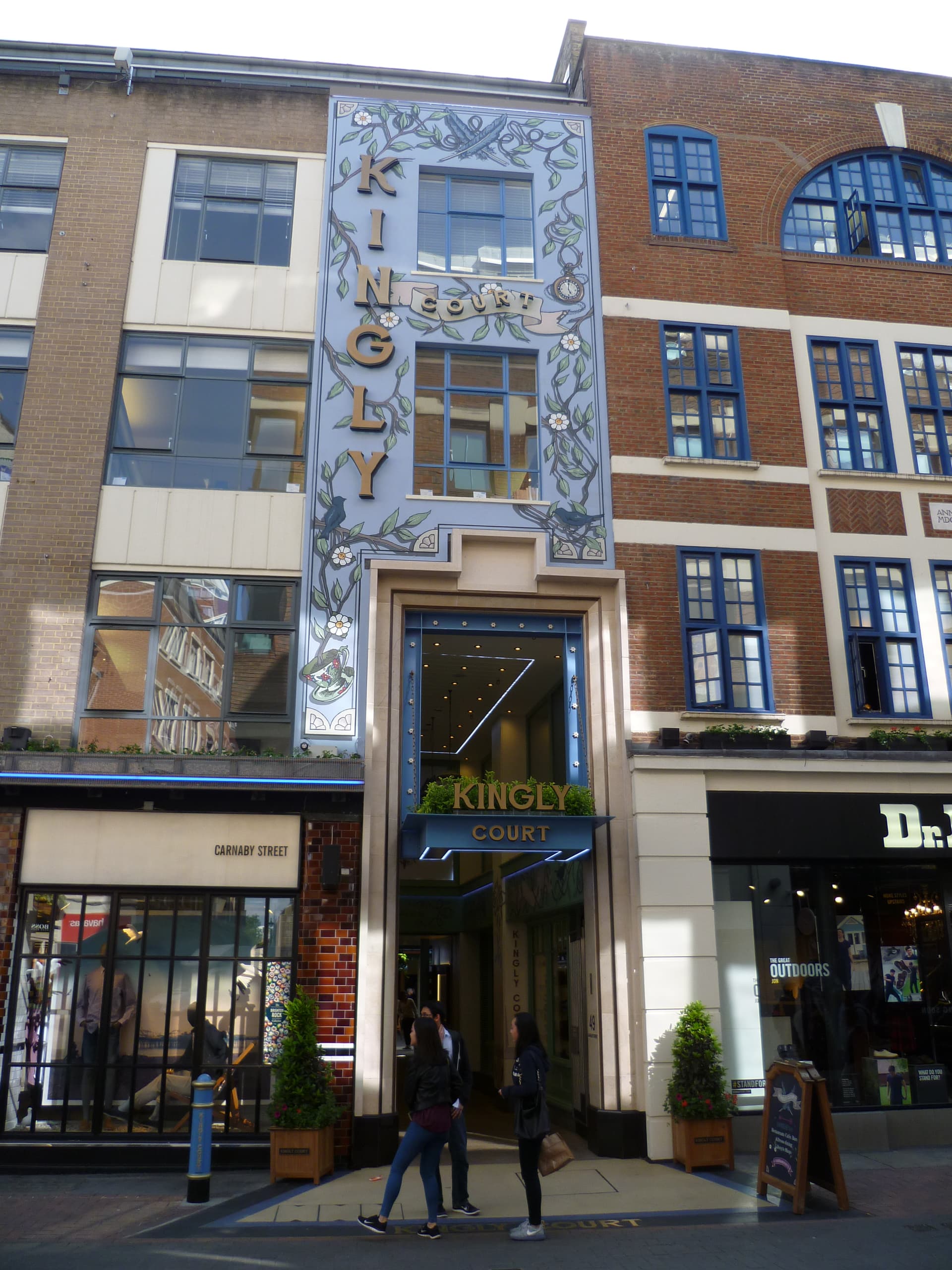 Decorated blue facade and entrance of Kingly Court off Carnaby Street, Soho, with passers-by outside