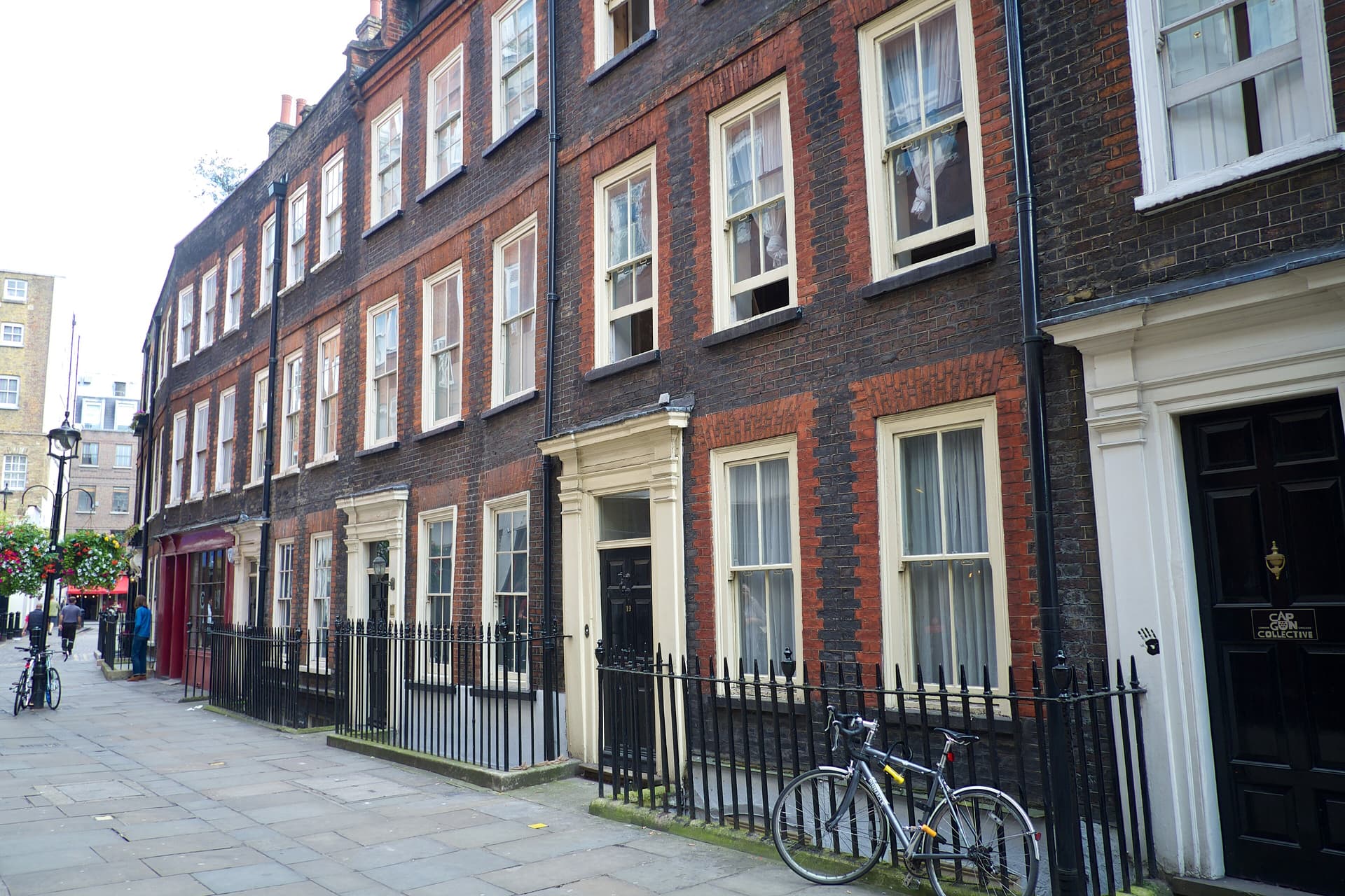 Terrace of dark Georgian brick houses with cream doorcases, sash windows and black iron railings on a Soho street
