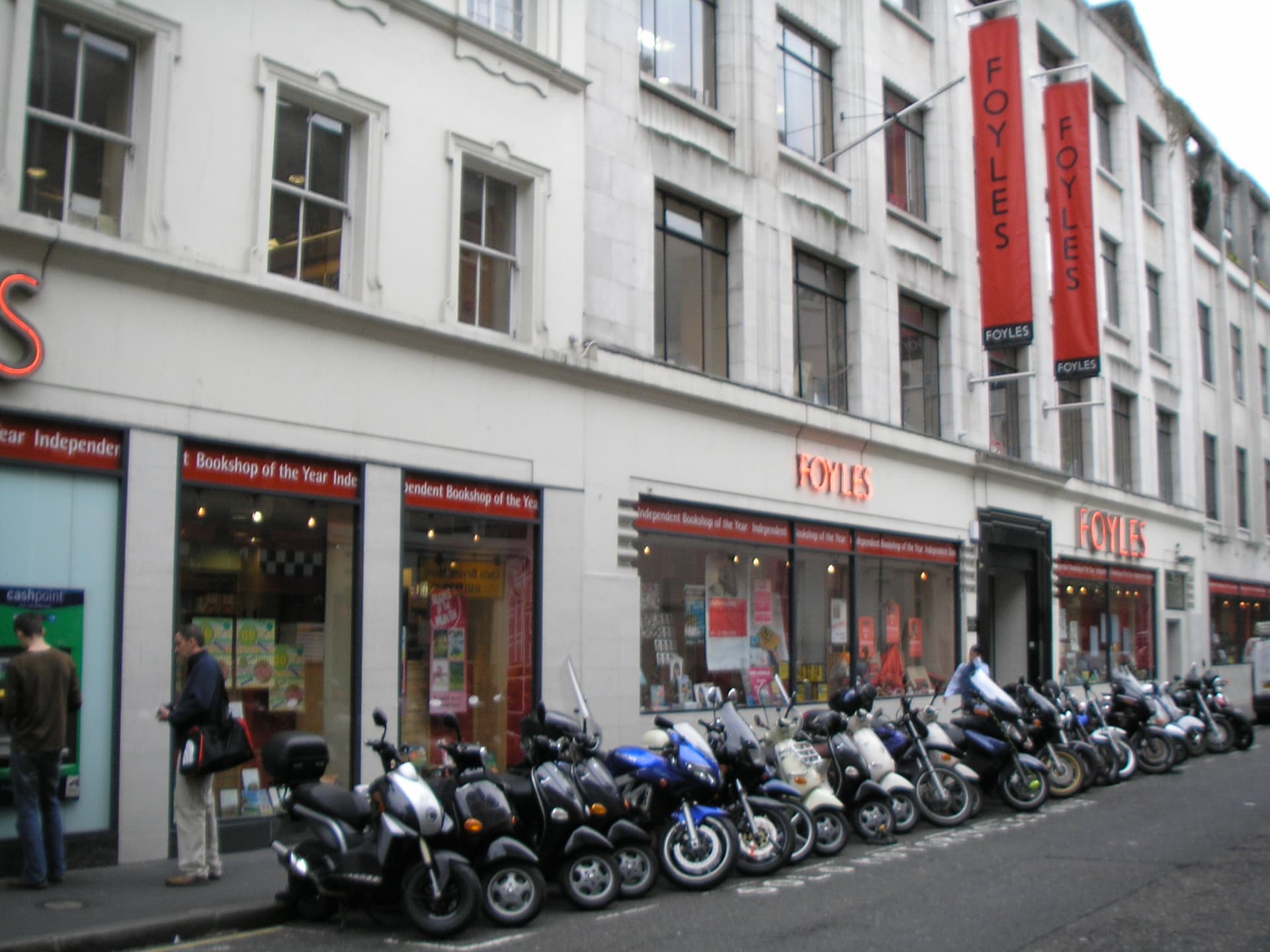 Row of parked motorbikes and scooters outside the white-fronted Foyles bookshop with red banners and neon signs