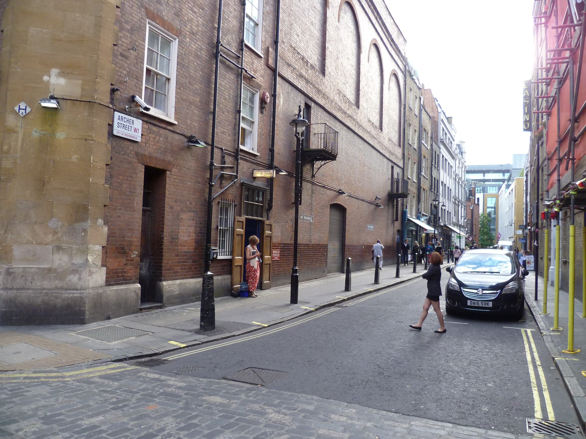 Brick theatre stage door and street sign on Archer Street, Soho, with pedestrians and a parked car