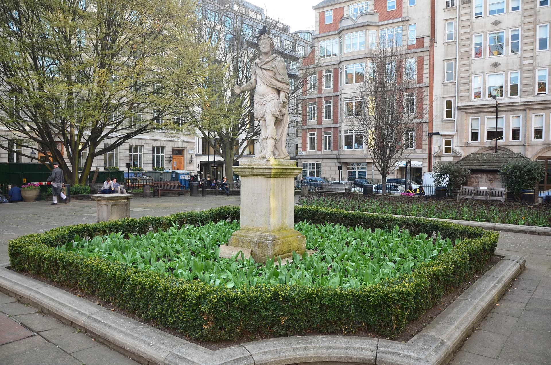 Stone statue of George II on a plinth amid tulip shoots and clipped box hedging in Golden Square