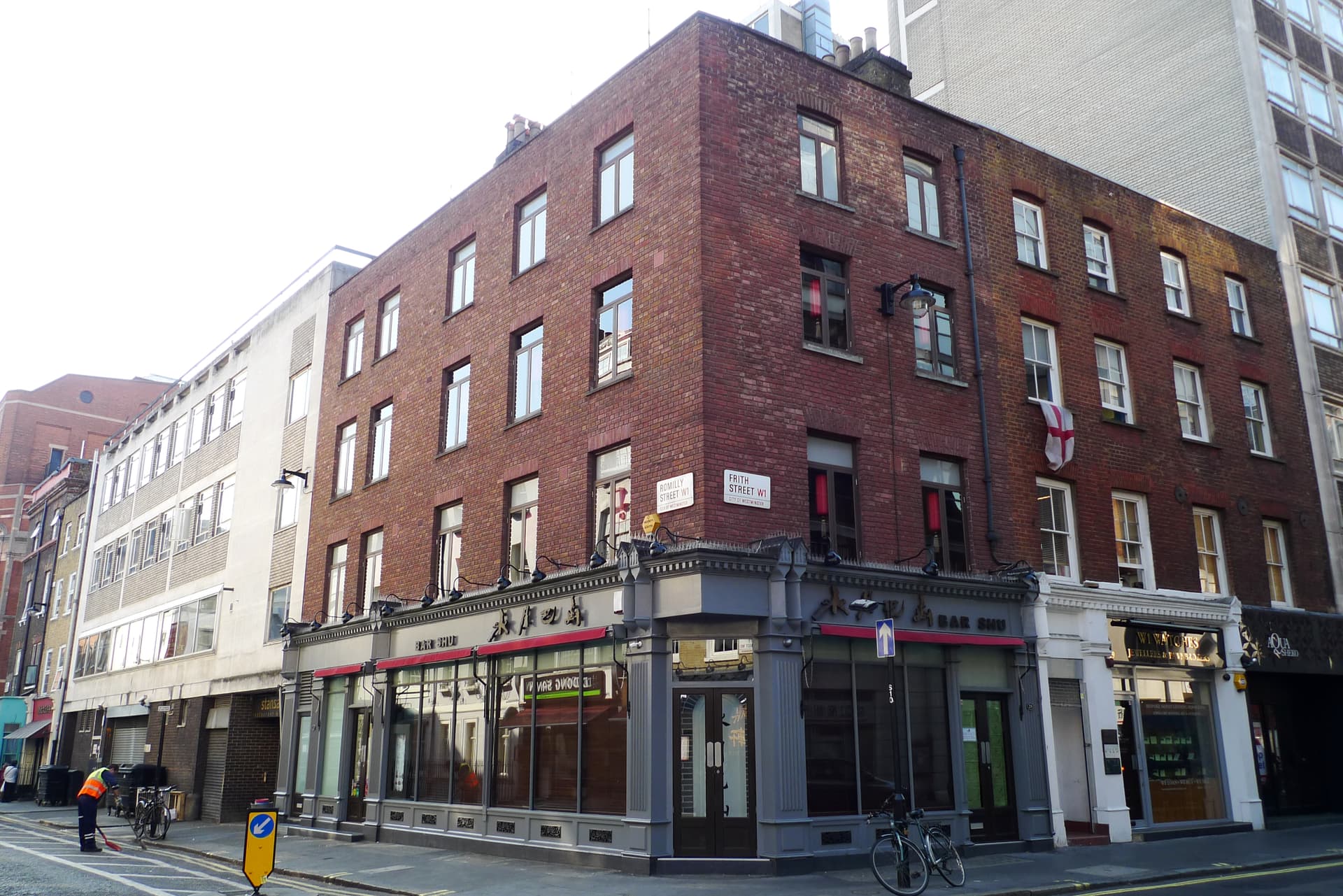 Red-brick corner building with grey shopfront at Romilly Street and Frith Street junction in Soho, London