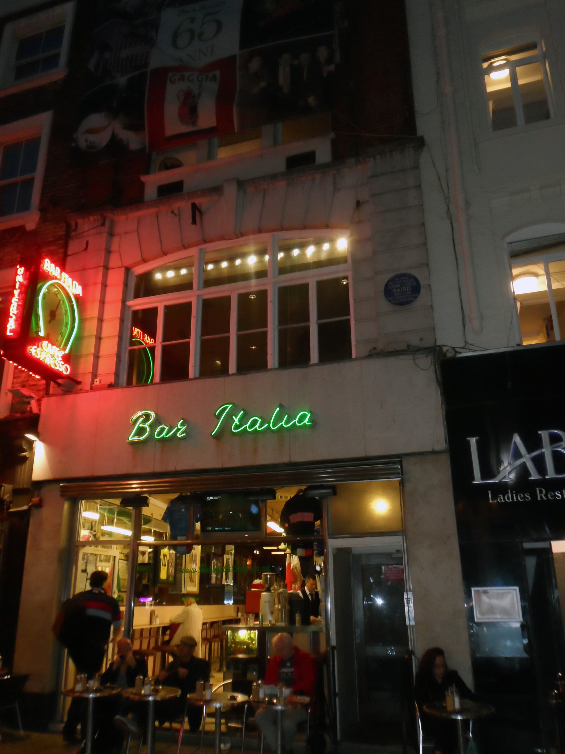 Neon-lit Bar Italia café frontage at night on Frith Street, Soho, with customers at outdoor tables