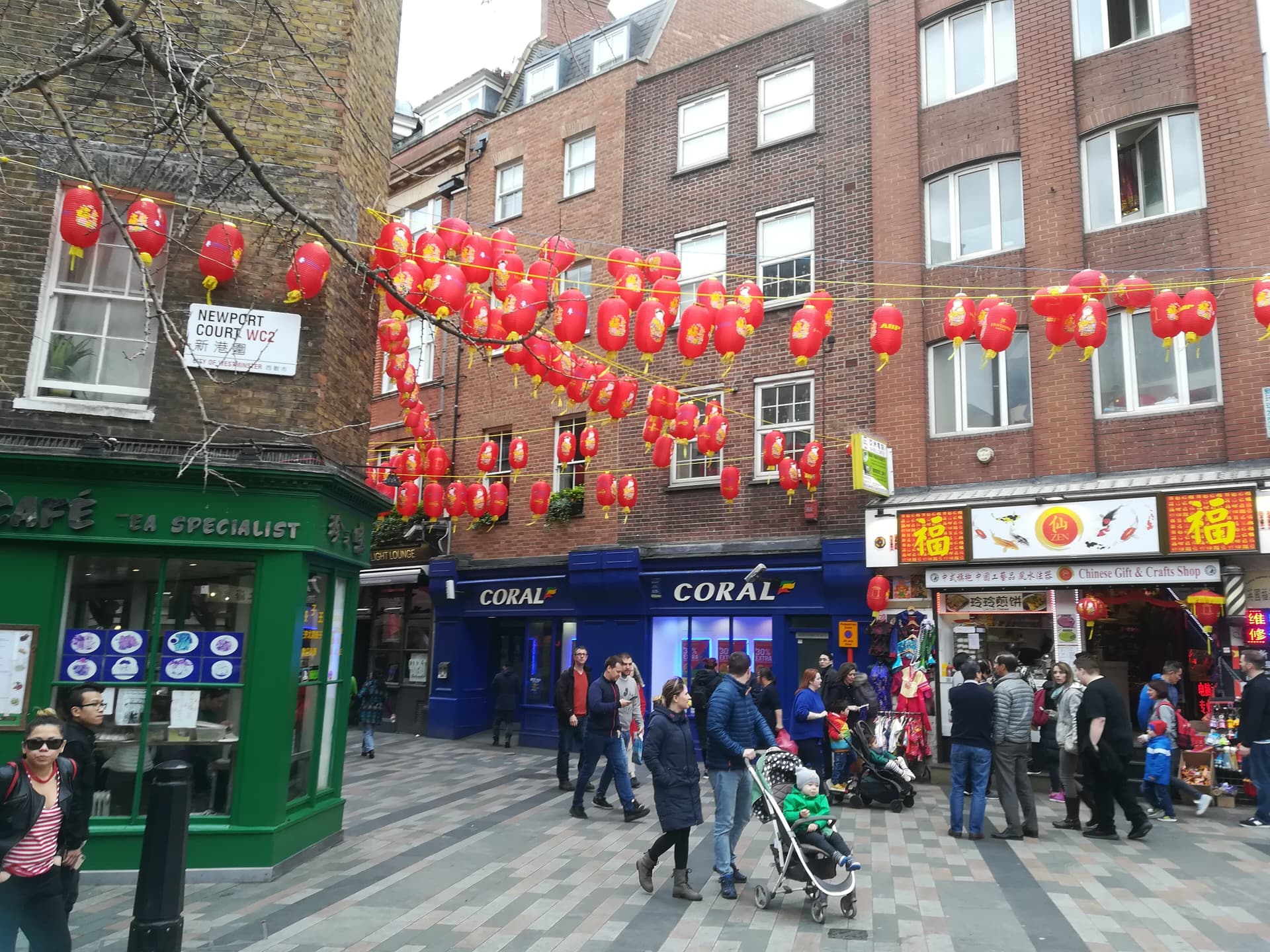 Red paper lanterns strung above Newport Court in Chinatown, with shops and pedestrians on a paved street