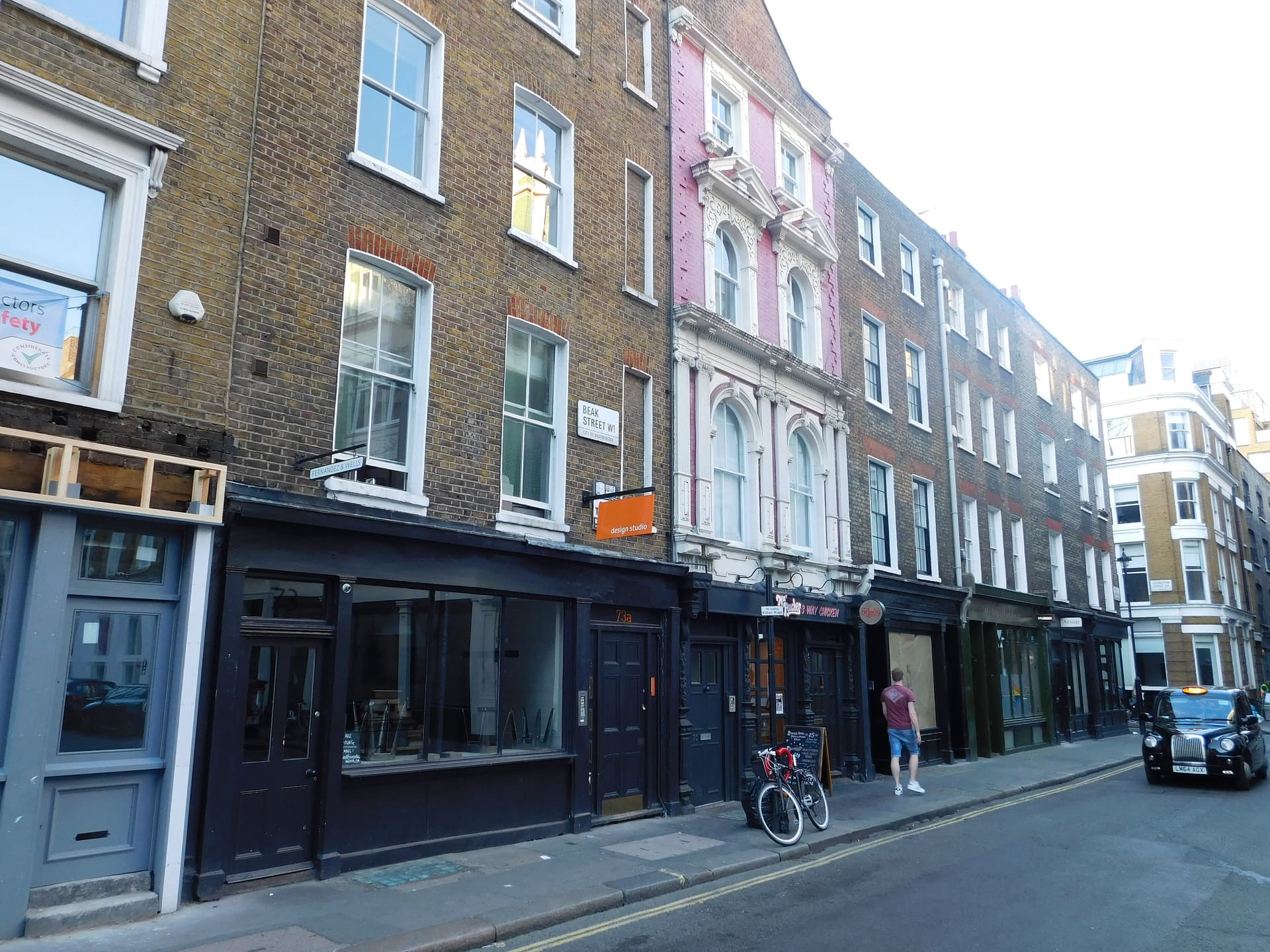 Georgian brick terrace and dark shopfronts on Beak Street, Soho, with a black taxi and parked bicycle