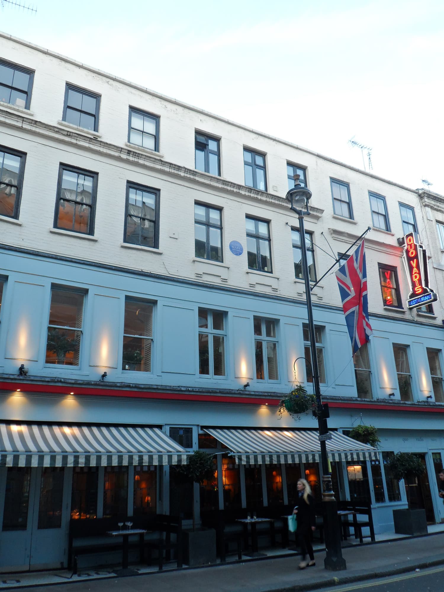 Pale blue and white Soho building with Quo Vadis neon sign, striped awnings, Union flag and blue plaque above
