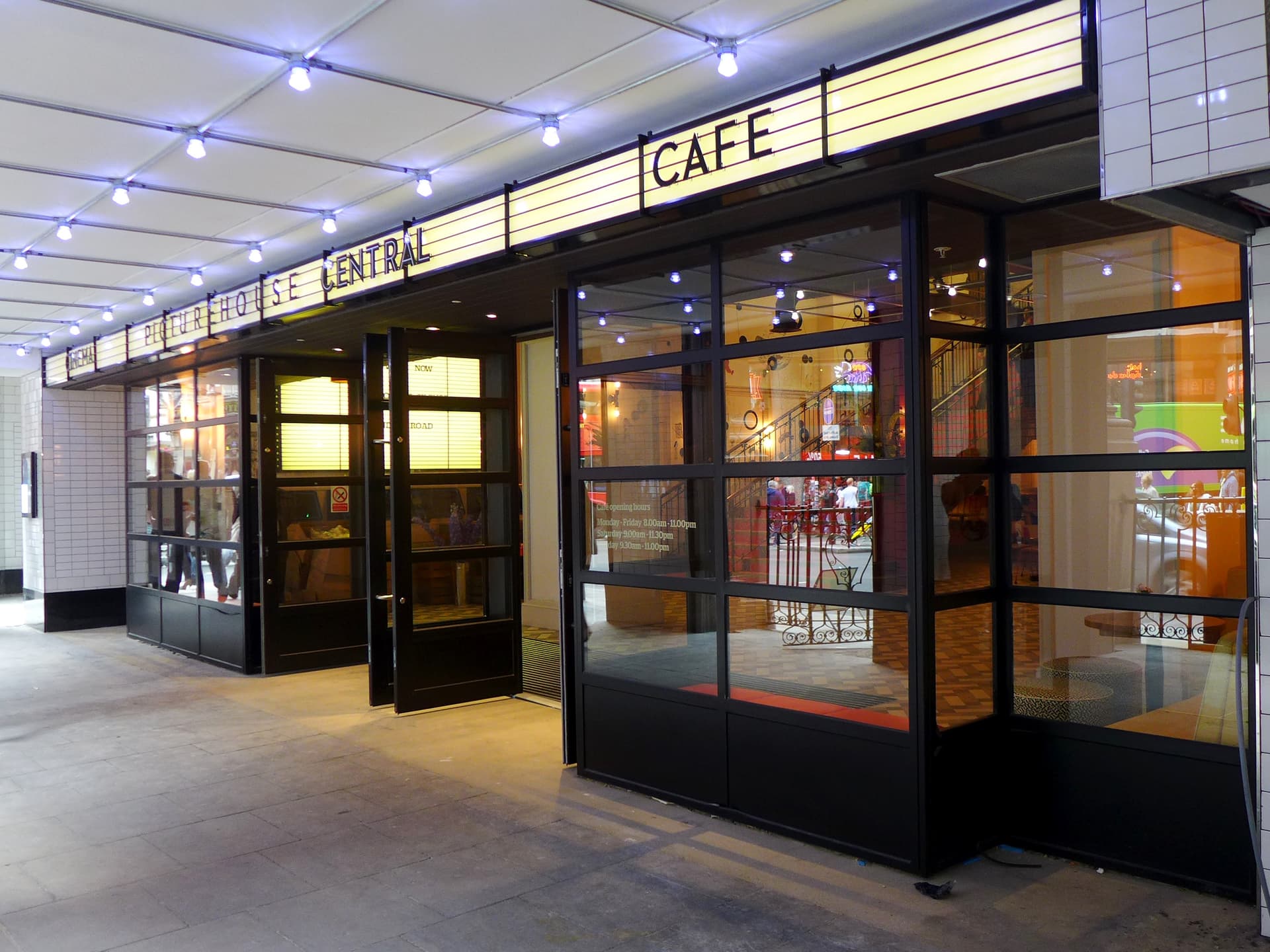 Illuminated entrance canopy and glazed café frontage of Picturehouse Central cinema on a Piccadilly Circus street at dusk