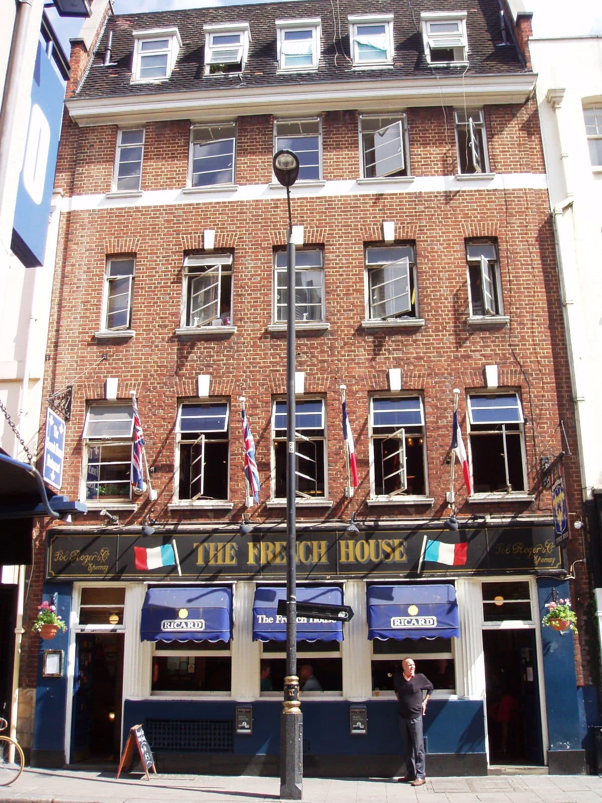 Red-brick frontage of The French House pub in Soho, with French and Union flags and blue Ricard awnings