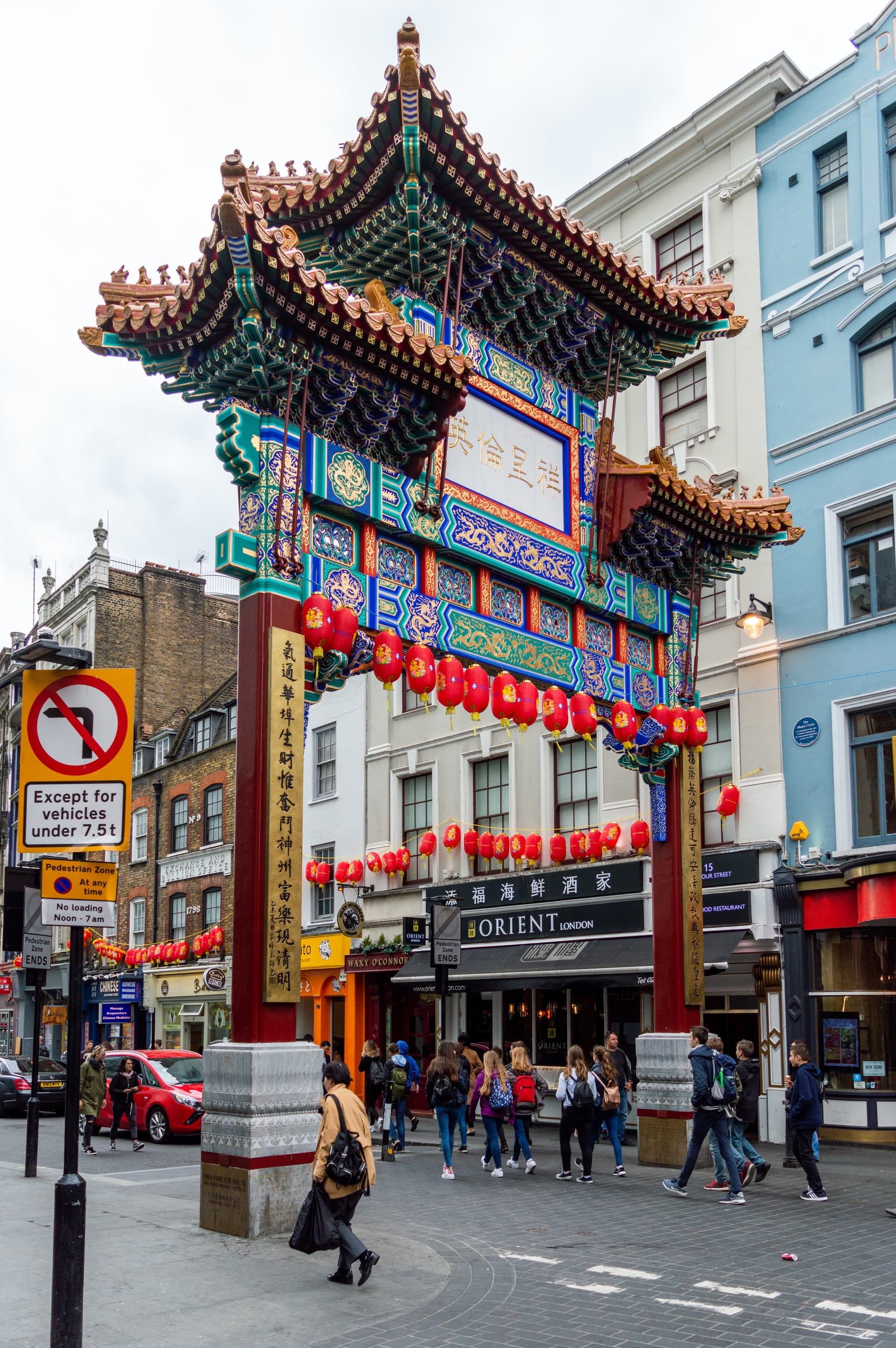 Ornate painted Chinese paifang gate hung with red lanterns above a Chinatown street in Soho, with pedestrians passing below