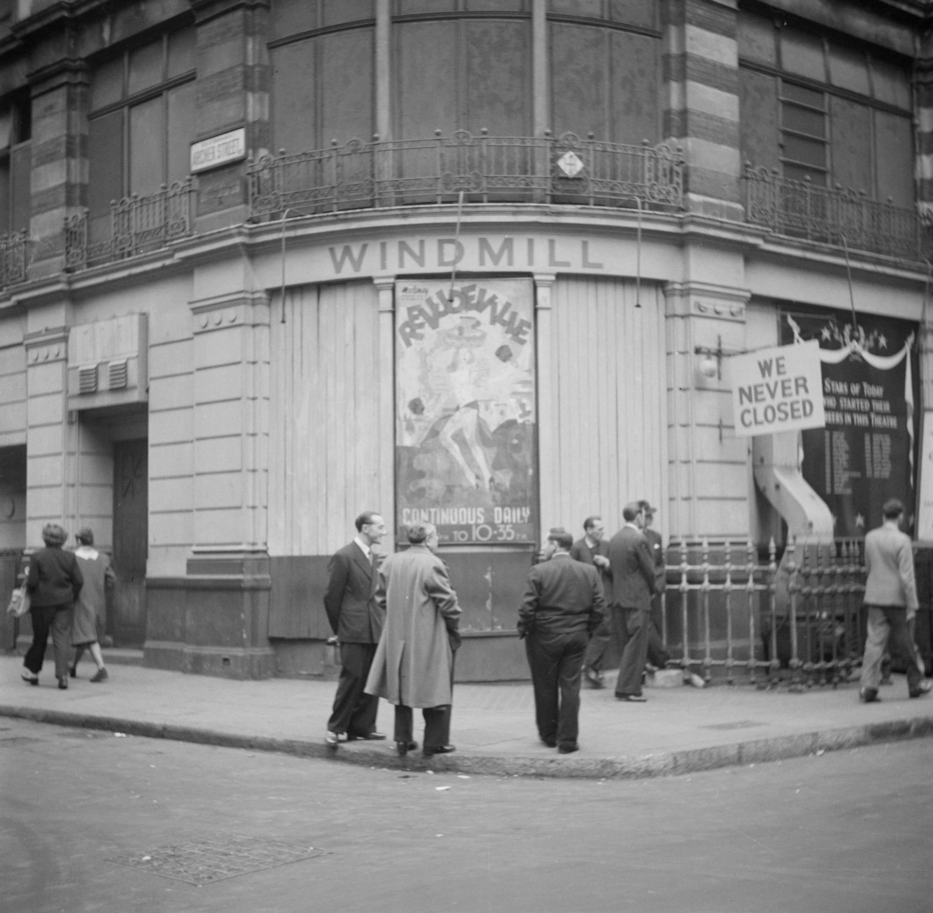 Black and white photograph of men standing on the corner of Archer Street outside the Windmill Theatre, Soho