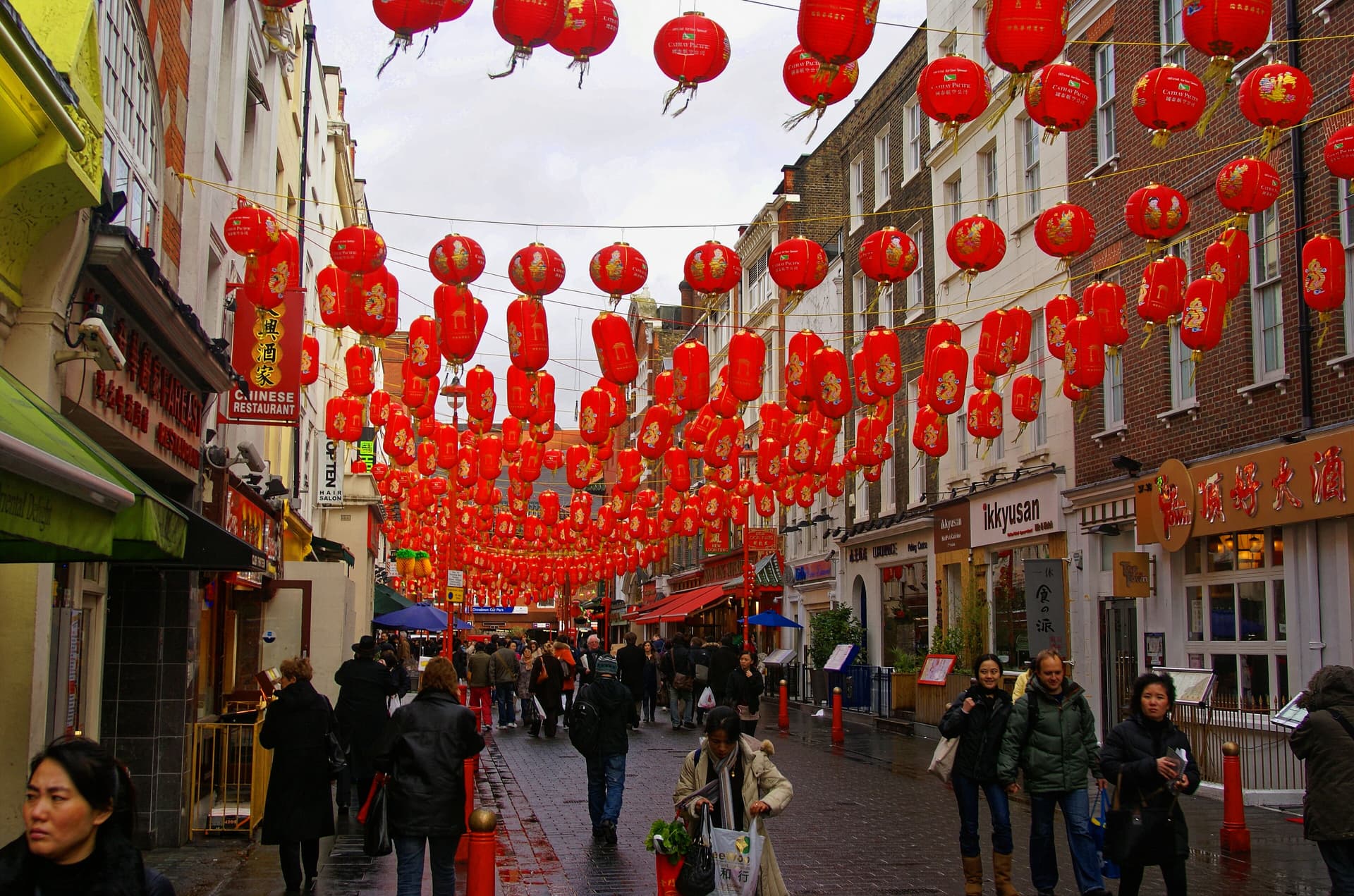 Red paper lanterns strung over a wet pedestrianised Chinatown street lined with restaurants and shoppers