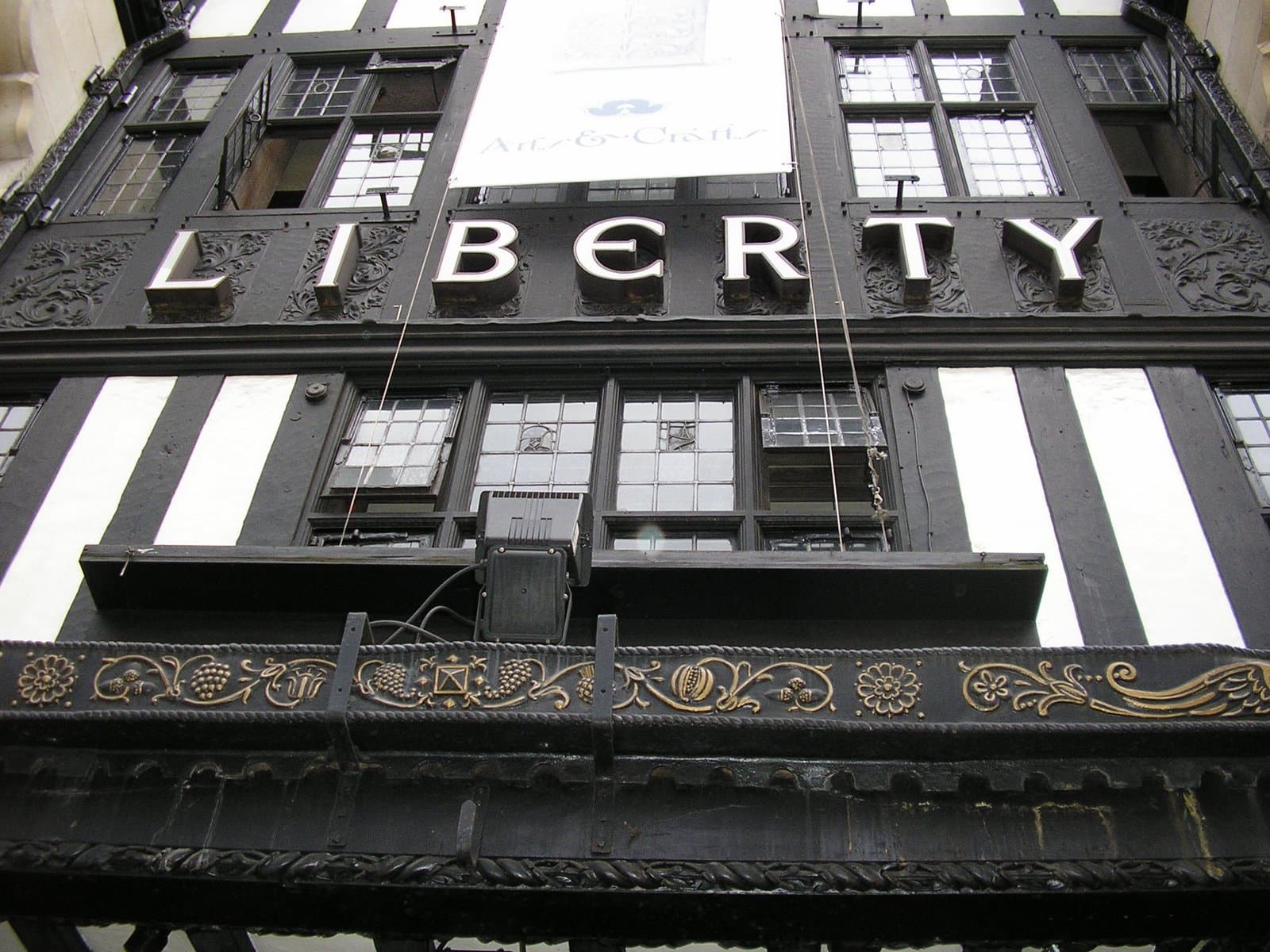 Looking up at Liberty's black and white timber-framed facade, with ornate gilded carving and the store name in white lettering